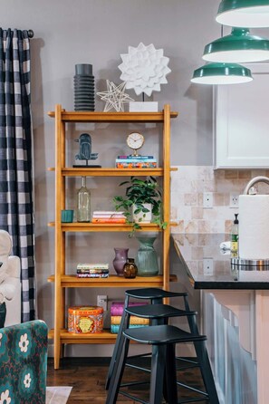 Una cocina con una estantería de madera, un reloj y una lámpara colgante verde.