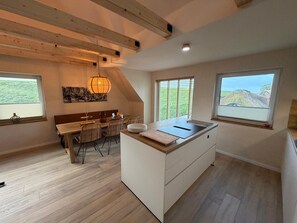 Eine moderne Küche mit Kochinsel, Holzboden und großen Fenstern, die einen Blick ins Freie ermöglichen.