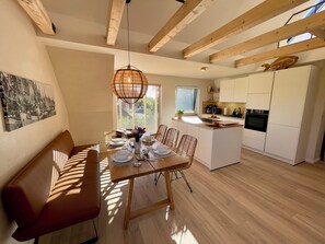 Eine moderne Küche mit Holzbalken, einem Essbereich mit einer Bank und Blick ins Freie.
