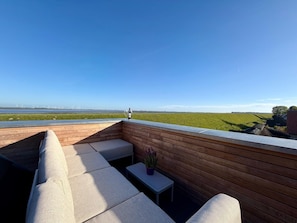 Eine Dachterrasse mit Blick auf ein grünes Feld und Windkraftanlagen in der Ferne.