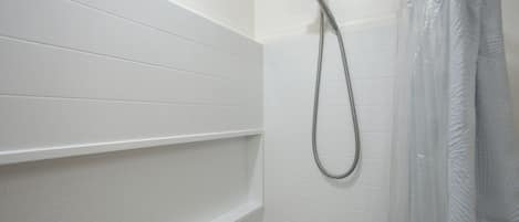 Ein Badezimmer mit weiß gefliesten Wänden, einer Dusche inklusive Duschhandstück und einem Duschvorhang.