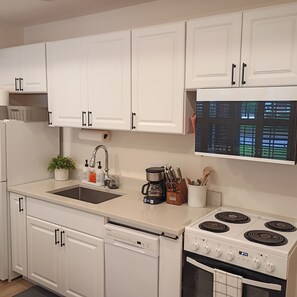 Una cocina con armarios blancos, un fregadero, una cafetera y una estufa.