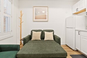 Ein Zimmer mit einem grünen Sofa, einem weißen Kühlschrank und einem gerahmten Bild an der Wand.