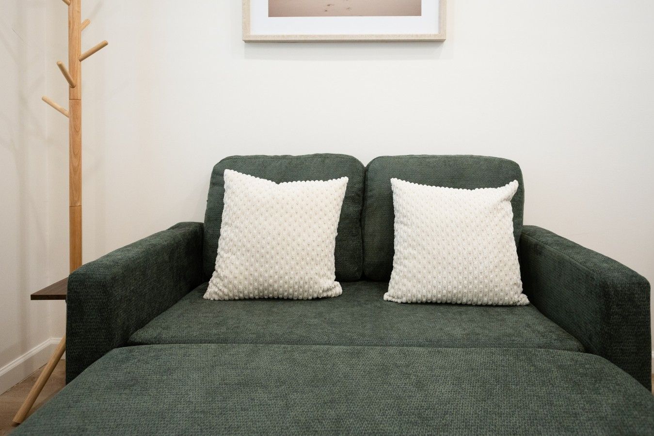 A green sofa with two white pillows and a framed picture on the wall.