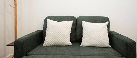 A green sofa with two white pillows and a framed picture on the wall.