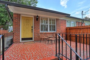 A house with a yellow door, a brick exterior, a wooden fence, and a tiled patio with outdoor furniture. - Cozy Guesthouse in Midtown Savannah (Savannah)