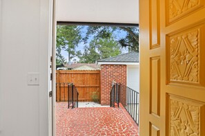 A view through a doorway into a backyard with a red-tiled patio, a wooden fence, and a brick wall. - Cozy Guesthouse in Midtown Savannah (Savannah)