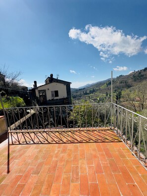 Eine Terrasse mit Fliesenboden, Metallgeländer und Blick auf einen Hügel mit einem Gebäude.