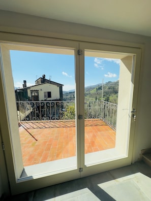 Eine Glastür führt zu einem Balkon mit Fliesenboden und Metallgeländer.