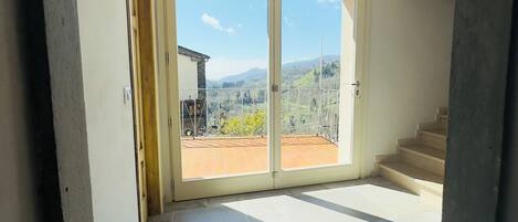 A room with a large sliding glass door leading to an outdoor terrace with a view of mountains.