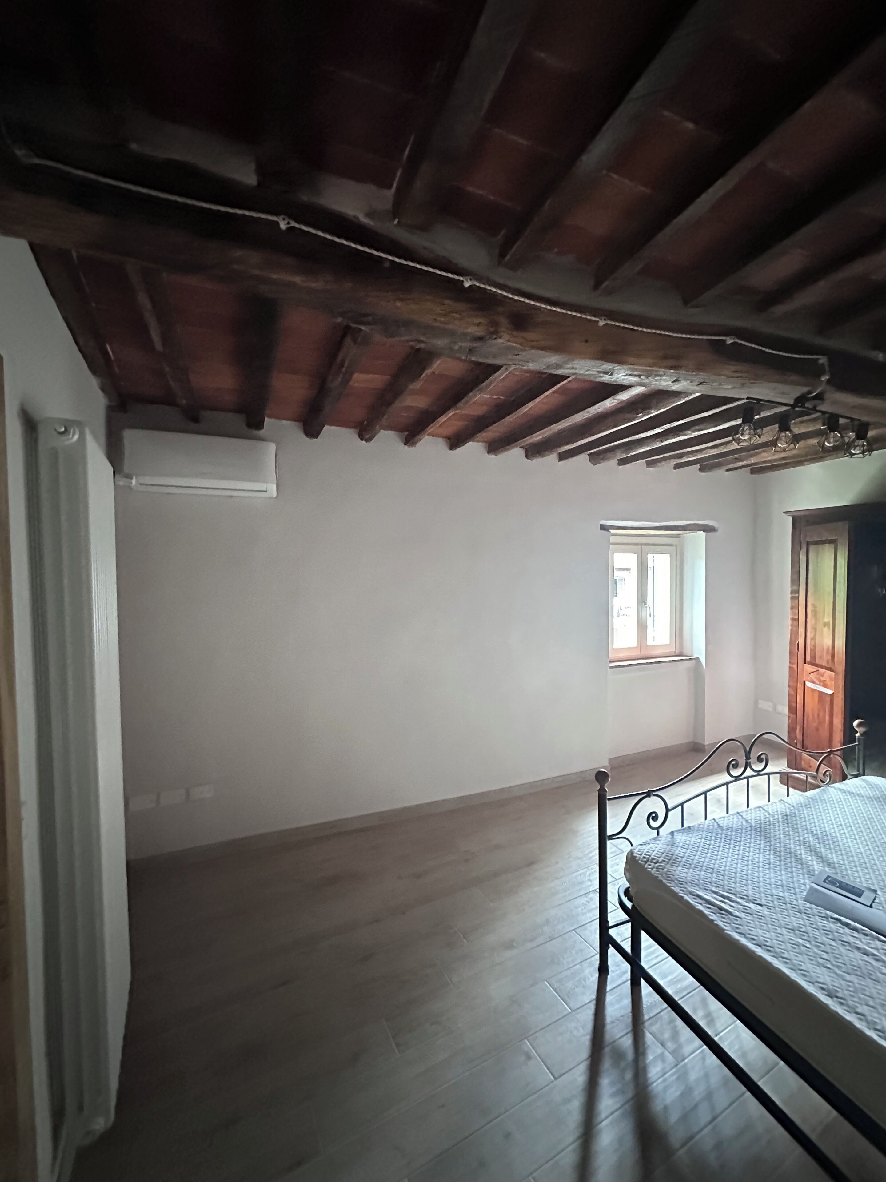 Une pièce avec un plafond en pente, un lit, une fenêtre et un radiateur.