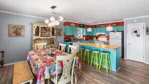 A compact kitchen with a central island, bar stools, and a dining table with chairs. - Snowbird-Friendly 3BR Gulf Shores Home Near Beach (Gulf Shores)