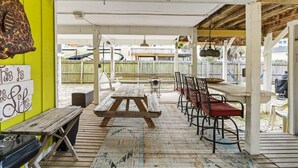 An outdoor patio with a wooden table and chairs, a bench, and a sign on the wall. - Snowbird-Friendly 3BR Gulf Shores Home Near Beach (Gulf Shores)