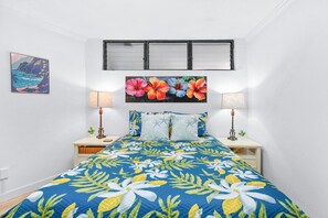 Ein Schlafzimmer mit einem Bett, zwei Nachttischen, einem Fenster und einem Wandbild.