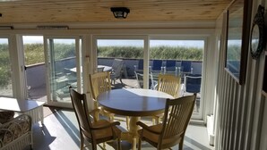 Un porche cubierto con una mesa redonda y sillas, puertas de cristal amplias que dan a vistas de la playa, y un cartel que dice 'HYDRANGEA BLUES'.