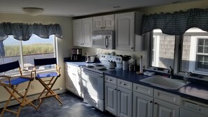Una cocina con armarios blancos, estufa, fregadero y ventana con cortinas.