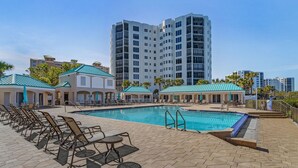 Uma piscina com espreguiçadeiras, um edifício com telhado verde e um prédio residencial alto ao fundo.