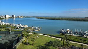 Uma marina com barcos atracados, quadra de tênis e vista para a água e edifícios ao longe.