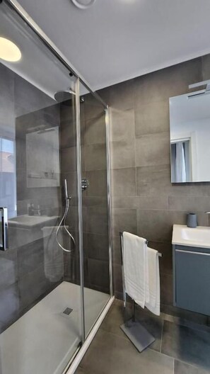Un baño moderno con ducha de vidrio, toallero blanco y un espejo grande sobre el lavamanos.