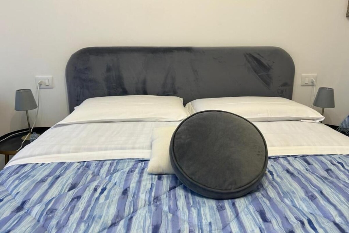 A bed with a grey headboard, white pillows, and a blue-striped bedspread.