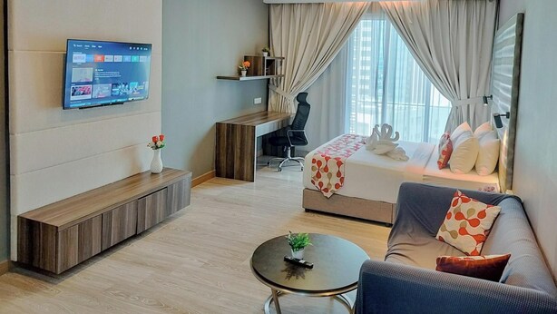 Une chambre d’hôtel moderne équipée d’un lit, d’un canapé, d’un téléviseur fixé au mur, d’un bureau et d’une fenêtre avec des rideaux.