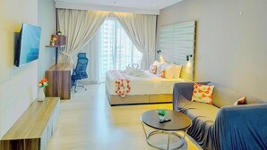 Une chambre d’hôtel comprenant un lit, un canapé, un bureau, une chaise, une télévision et une fenêtre avec des rideaux.