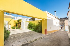 Una estrecha calle empedrada con un toldo amarillo, edificios blancos y vegetación.