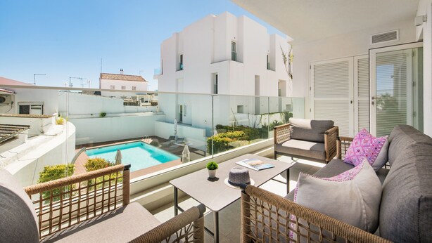 Ein Balkon mit Pool, Korbmöbeln und einem weißen Gebäude im Hintergrund.
