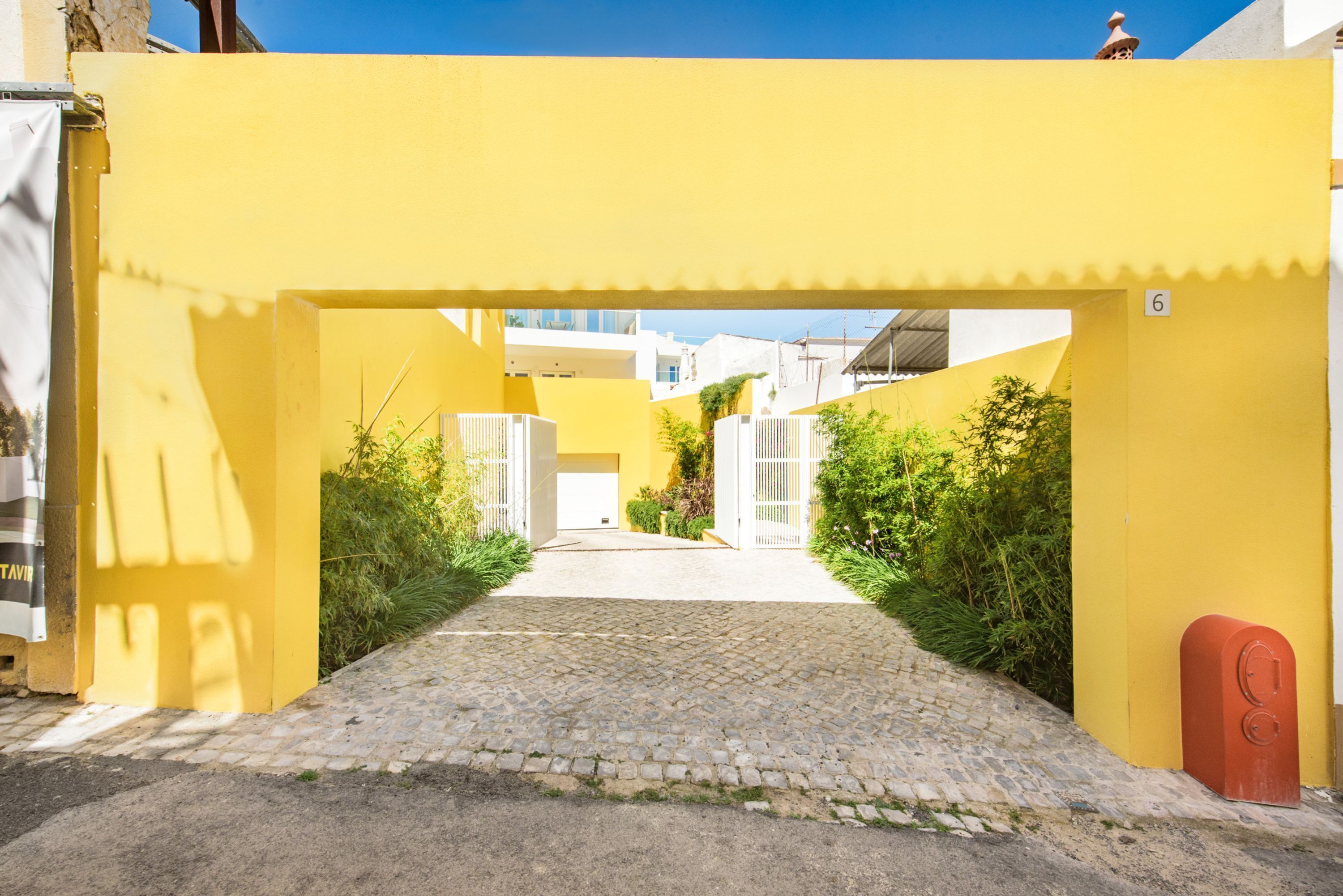 A yellow building with a cobblestone path leading to a white door, surrounded by greenery.