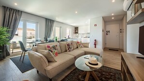 Ein modernes Wohnzimmer mit einer Couch, einem Glastisch und einem Essbereich im Hintergrund.