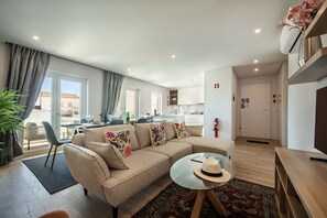 Una sala moderna con un sofá, una mesa de centro de vidrio y un comedor al fondo.
