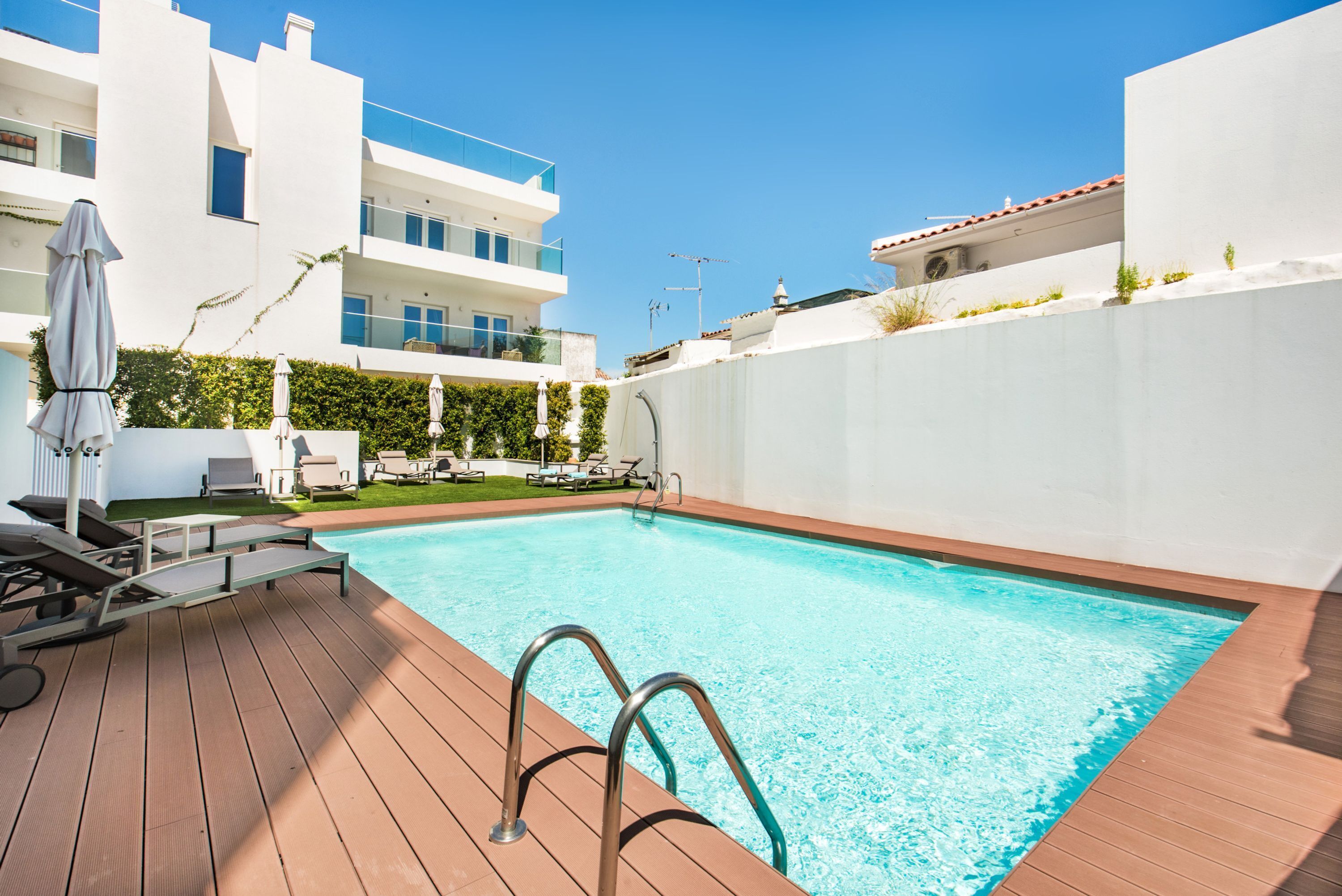A swimming pool with a wooden deck, lounge chairs, and umbrellas.
