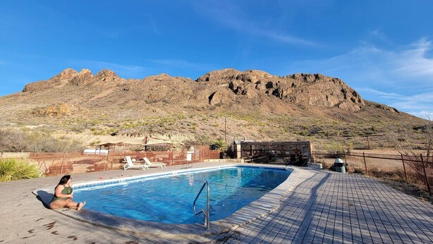 Una piscina con un pontile in legno, una persona seduta a bordo e montagne sullo sfondo.