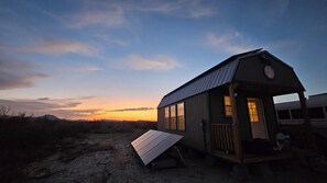 Eine kleine Hütte mit Veranda, Tisch und Blick auf den Sonnenuntergang.