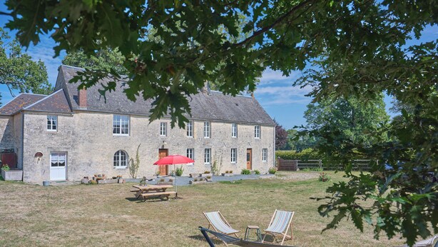 Un bâtiment en pierre avec une cour verdoyante, un hamac et une table de pique-nique.