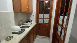 A narrow kitchen with wooden cabinets, a sink, and a door with frosted glass panels. - Beluna City Apart (Marmara)