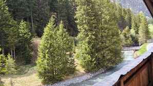 A wooden balcony overlooking a river with a forest and mountains in the background. - Rustic Pitztal alpine house by the stream with large balcony and garage (Sankt Leonhard im Pitztal)
