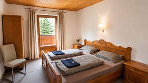 A bedroom with a wooden bed, a chair, a nightstand, a lamp, and a window with curtains. - Rustic Pitztal alpine house by the stream with large balcony and garage (Sankt Leonhard im Pitztal)