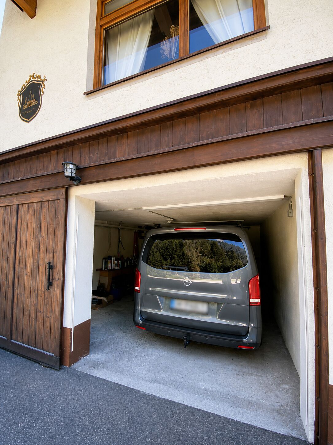 Un coche estacionado en un garaje con puerta de madera y ventana con cortinas.