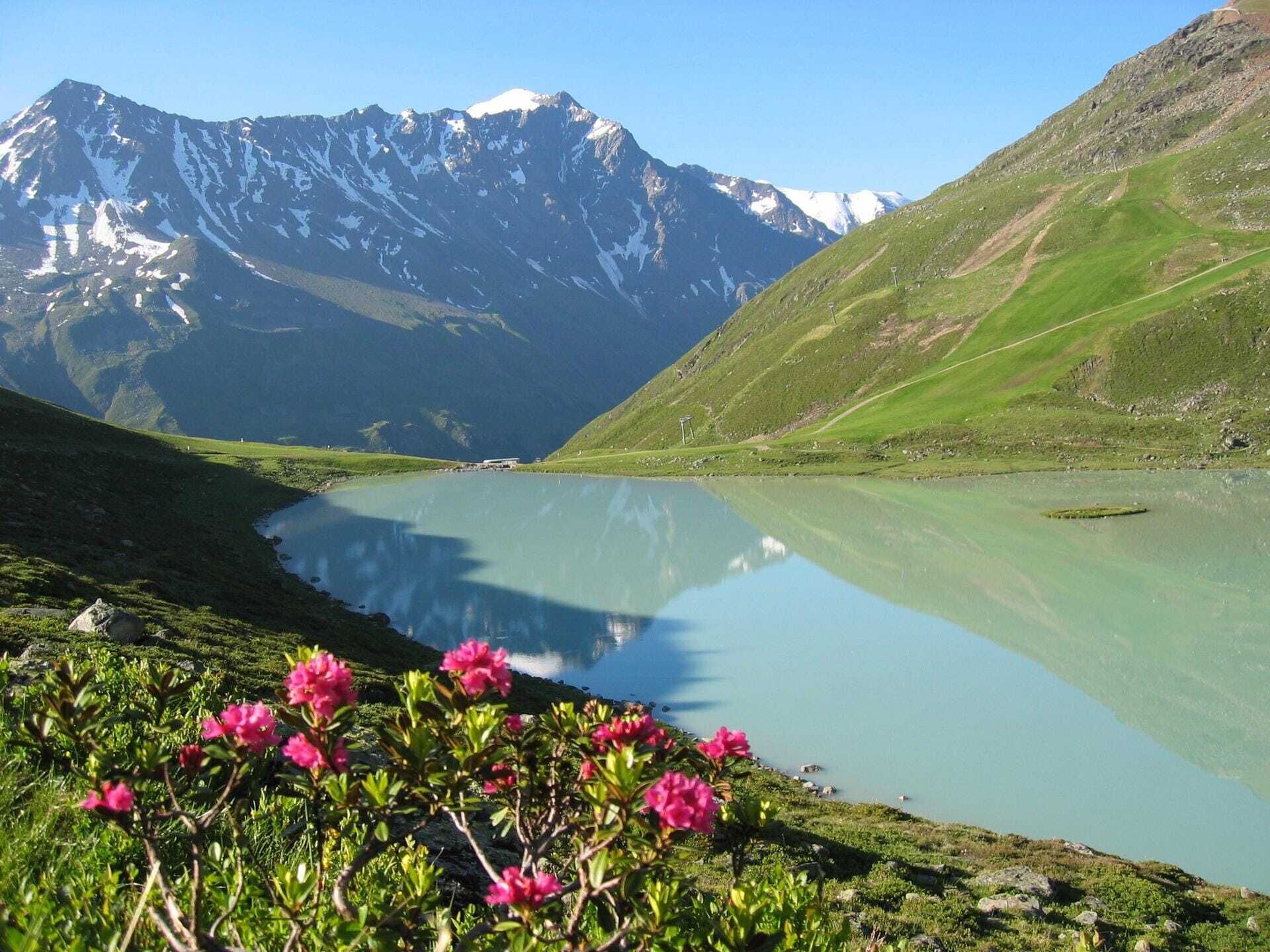 Un lago de montaña con reflejos, rodeado de colinas verdes y un cielo despejado.