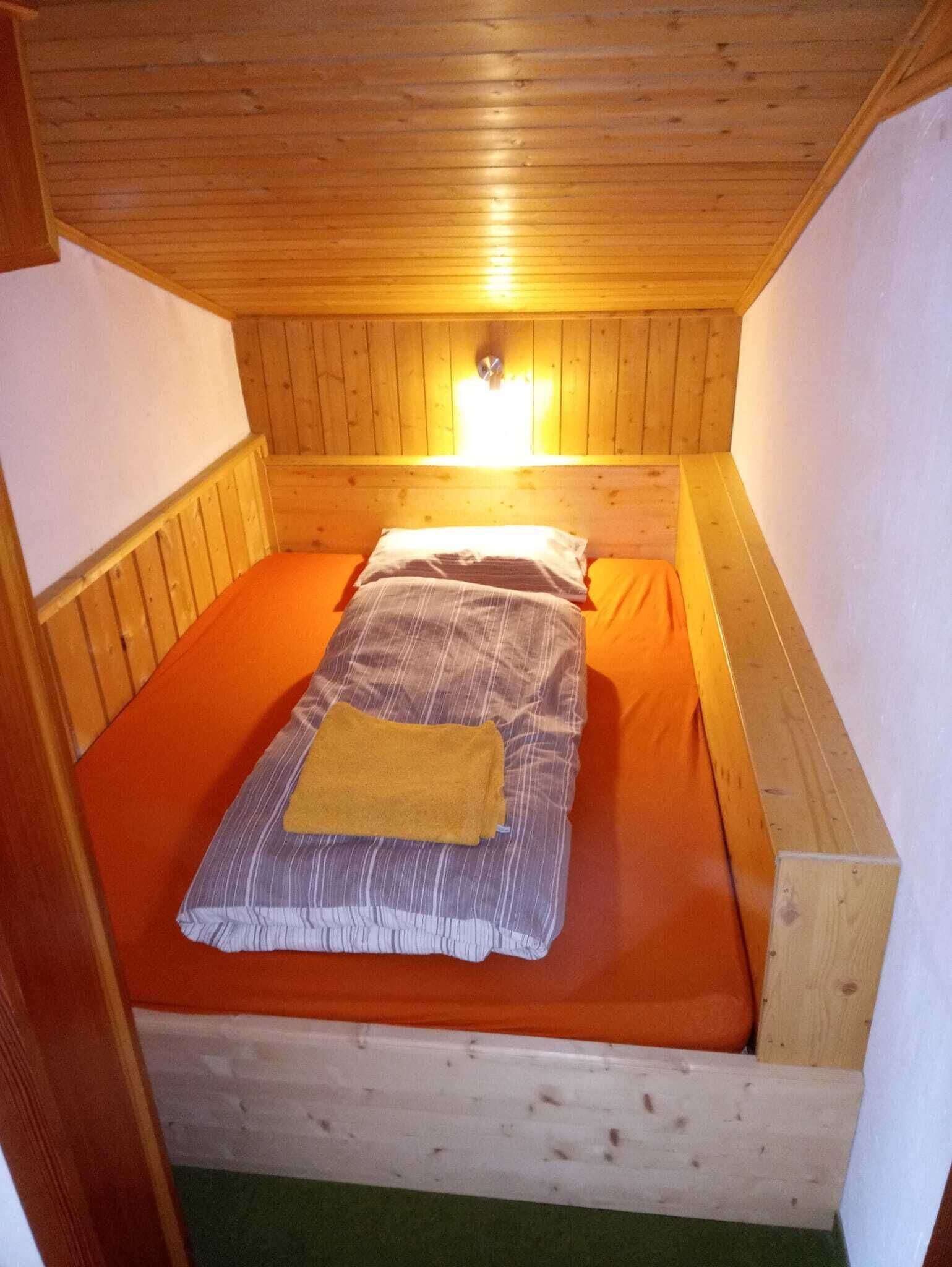 A small, single-bed room with wooden walls and a sloped ceiling.