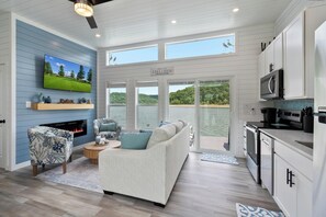 A modern living room with a fireplace, a large sofa, and a television displaying a golf course. - Lake'n Memories - The Ultimate Oasis Getaway (Russell Springs)