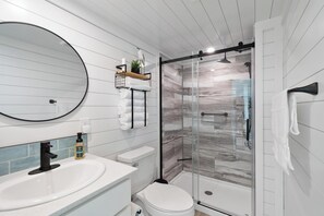 A modern bathroom with a round mirror, white tiles, a glass shower enclosure, and a white toilet. - Lake'n Memories - The Ultimate Oasis Getaway (Russell Springs)