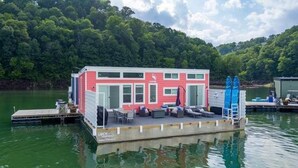 Una casa sull'acqua galleggiante con un pontile, posti a sedere all'aperto e una scaletta.