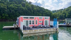 Ein schwimmendes Hausboot mit einer Anlegestelle, Sitzgelegenheiten im Freien und einer Leiter.
