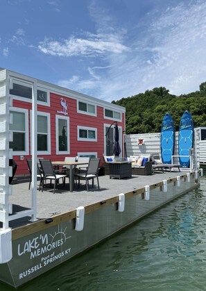 Un edificio frente al agua con zona de comedor, sillas de descanso y kayaks.