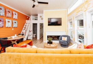 A living room with a sofa, a fireplace, a TV, and a dining area with a table and chairs. - First Light - Modern Floating Home Designed for Elevated Lake Living (Russell Springs)
