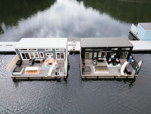 Two floating houses with outdoor seating areas, a pool, and a small boat docked nearby. - First Light - Modern Floating Home Designed for Elevated Lake Living (Russell Springs)