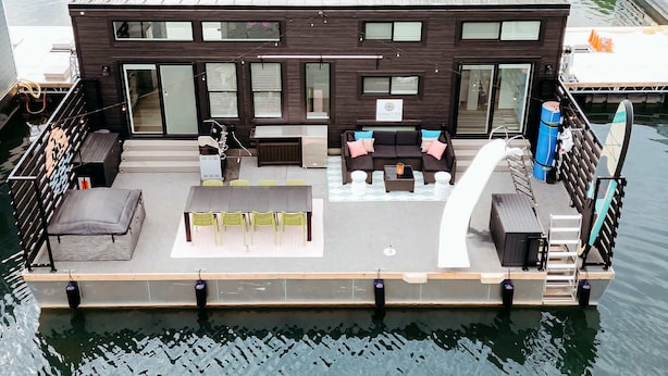 A floating house with a deck, outdoor seating, and a small table.