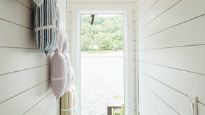 A narrow hallway with white wooden walls and a window leading to a beach view.